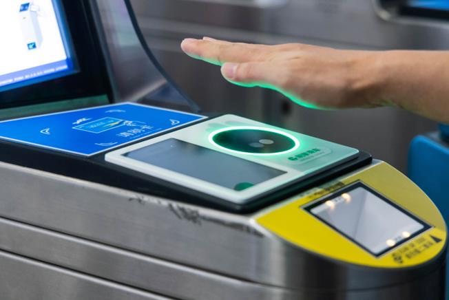 Close-up of commuter scanning palm at Daxing Metro turnstile — hand hovering over the green-lit palm recognition sensor for contactless fare payment